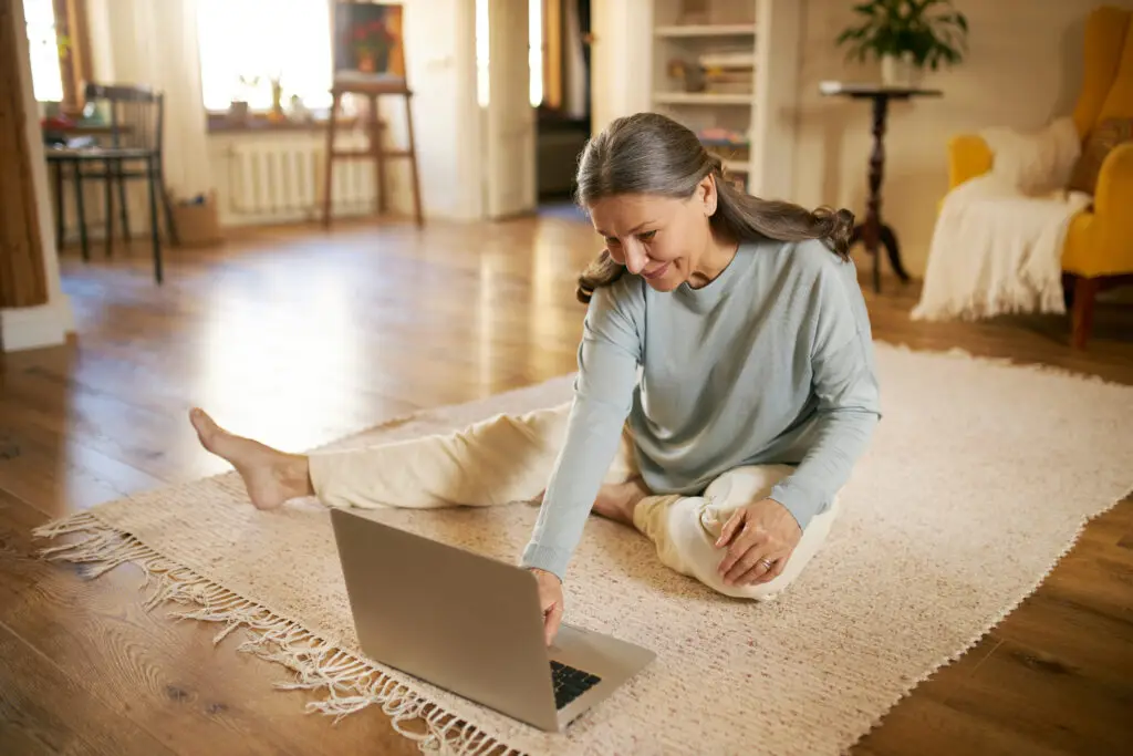 Middle-aged woman sitting on the floor, enjoying the underfloor heating, while working on laptop in a modern home